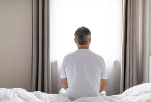 hombre sentado en la cama viendo hacia la vetana cerrada