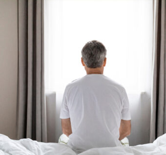 hombre sentado en la cama viendo hacia la vetana cerrada